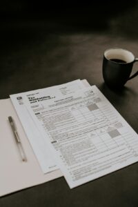 A person sorts tax forms, receipts, and labeled folders at a home desk.