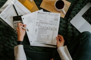 Person reviewing tax forms and receipts at a home desk with a calculator and organized documents.