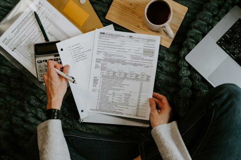 Person reviewing tax forms and receipts at a home desk with a calculator and organized documents.